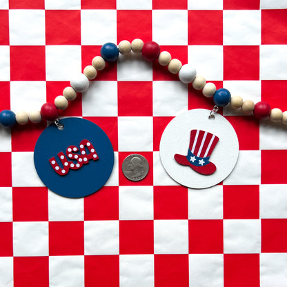 Happy 4th of July Handmade Garland. Features patriotic-themed shapes - a star, a "USA" and a 4th of July wood cutout, Uncle Sam's hat, and a firecracker. Summer red, white, blue decor and gifts.