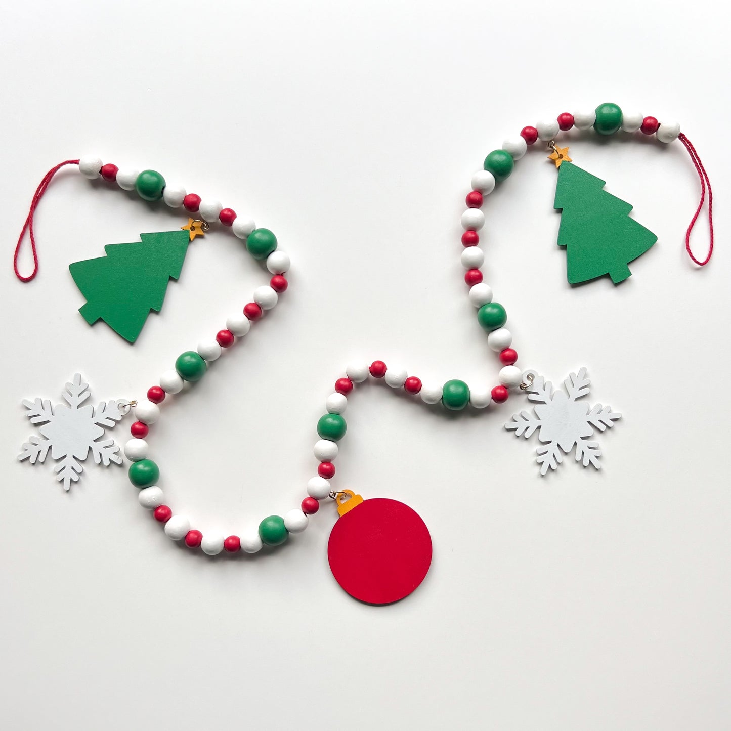 Holiday Cheer Handmade Garland. The garland features two decorated Christmas trees, two snowflakes, and one red ornament with a gingerbread man. Shapes hang from wood beads. Christmas holiday seasonal decoration or gift.