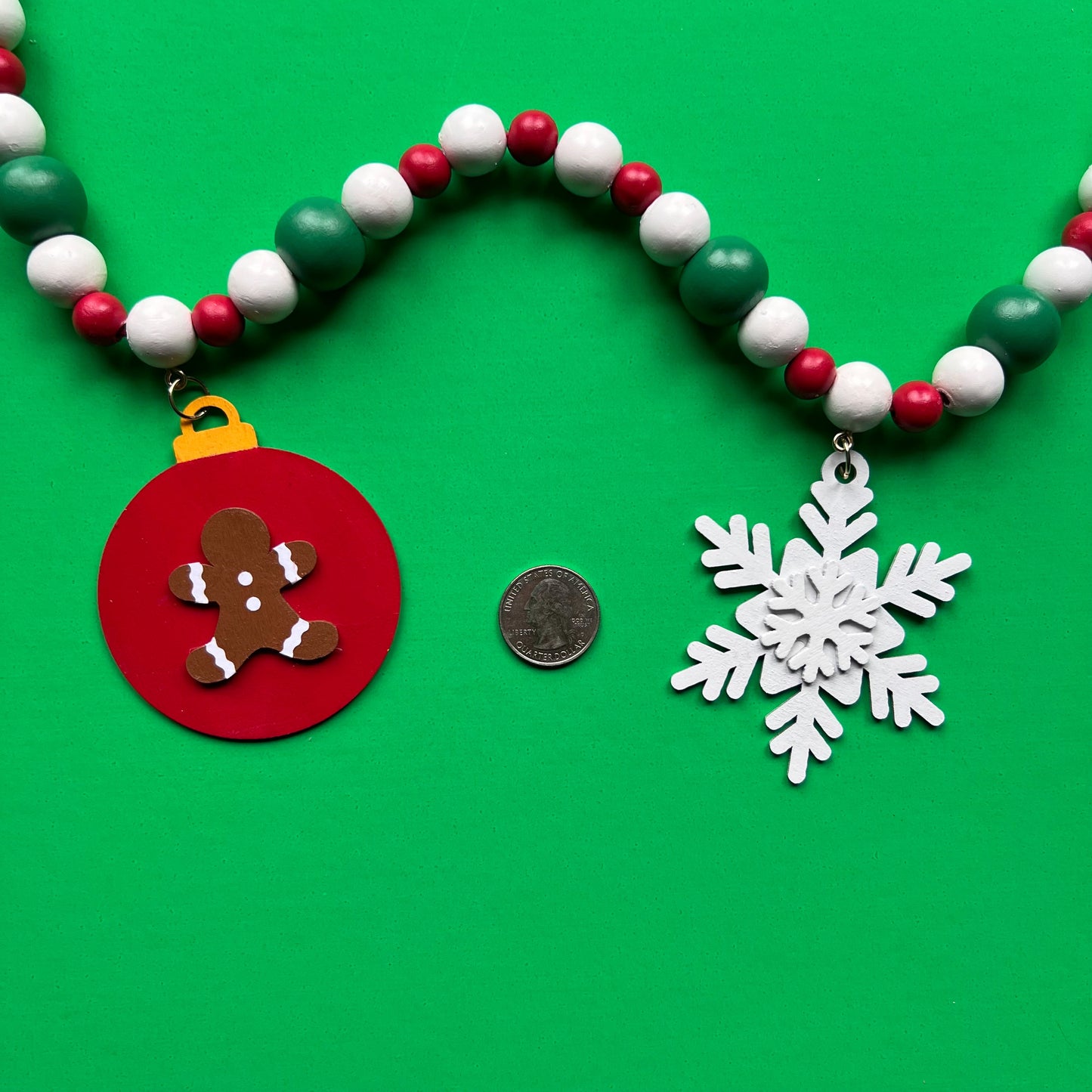 Holiday Cheer Handmade Garland. The garland features two decorated Christmas trees, two snowflakes, and one red ornament with a gingerbread man. Shapes hang from wood beads. Christmas holiday seasonal decoration or gift.