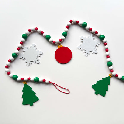 Back of a Christmas themed wood bead garland with beads painted green, red or white. 5 shapes hang from beads painted those same colors - 2 green trees, 2 white snowflakes and 1 red ornament with a gingerbread man on the front. Garland is displayed on a white background.