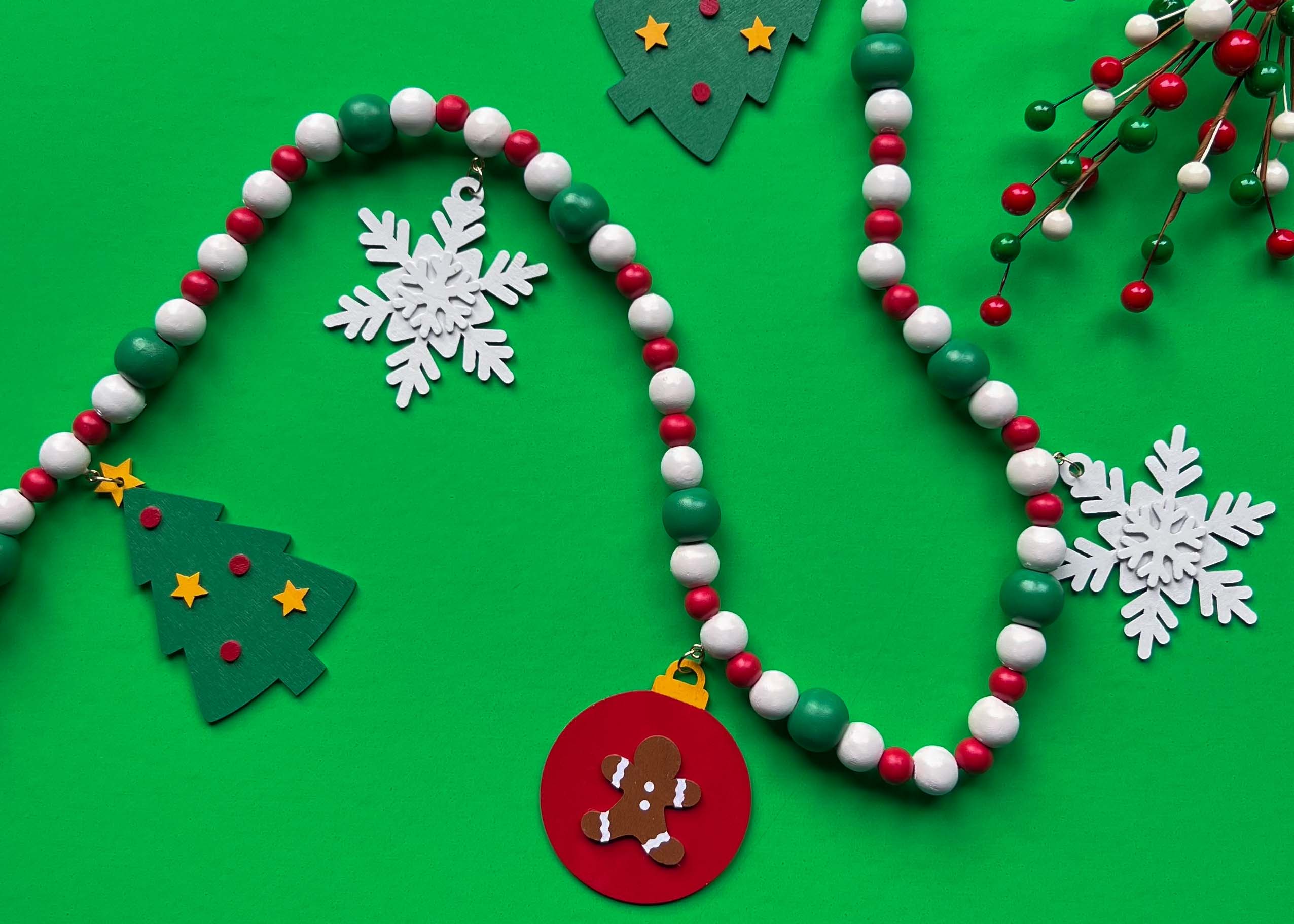 Christmas themed wood bead garland with snowflakes, trees, and an ornament with a gingerbread man hanging from beads.