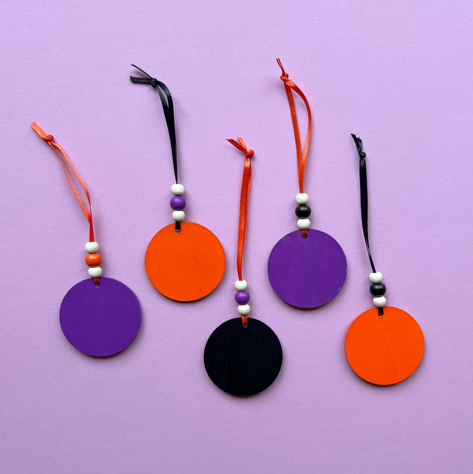 Set of 5 small wood Halloween ornaments. Feature 2 inch wood circles with Halloween themed shapes. Include three wood beads with a ribbon.