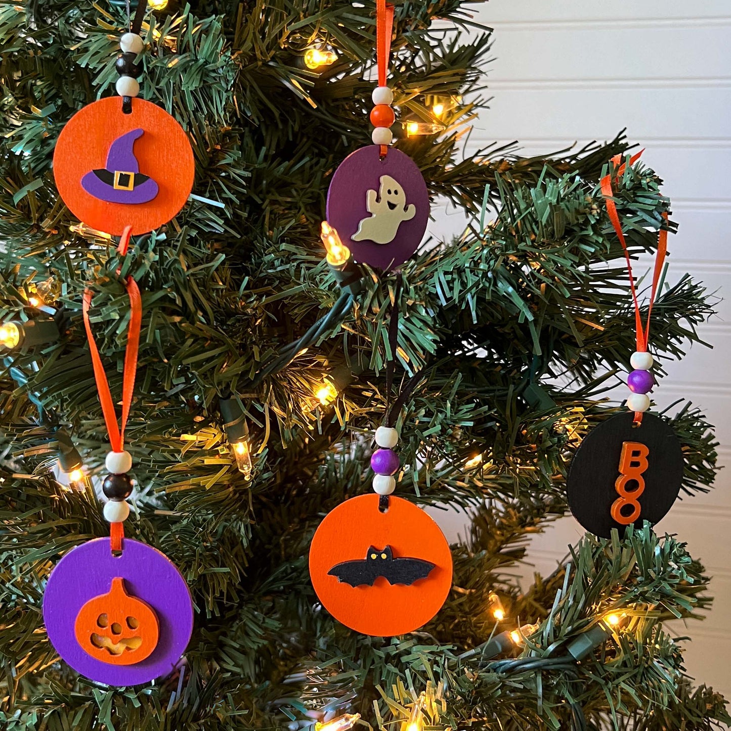 Set of 5 small wood Halloween ornaments. Feature 2 inch wood circles with Halloween themed shapes. Include three wood beads with a ribbon.