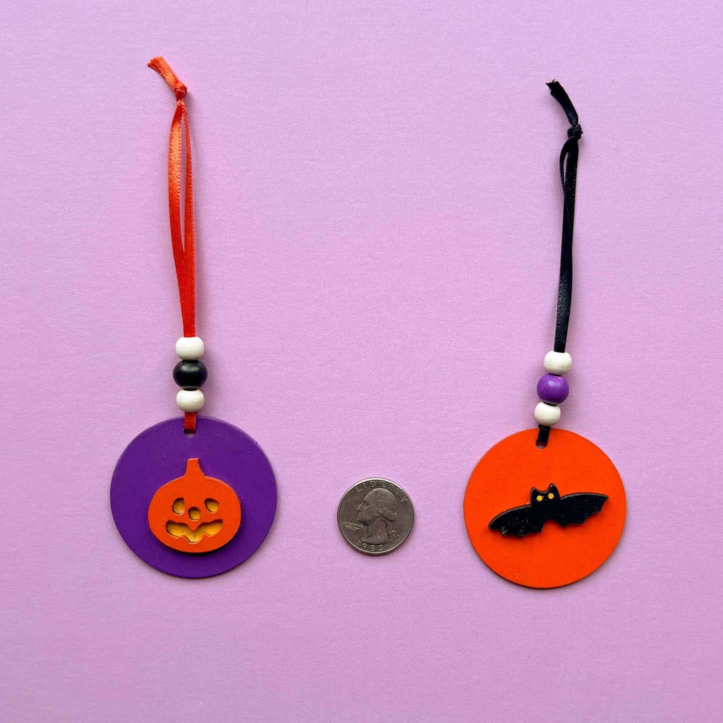 Set of 5 small wood Halloween ornaments. Feature 2 inch wood circles with Halloween themed shapes. Include three wood beads with a ribbon.