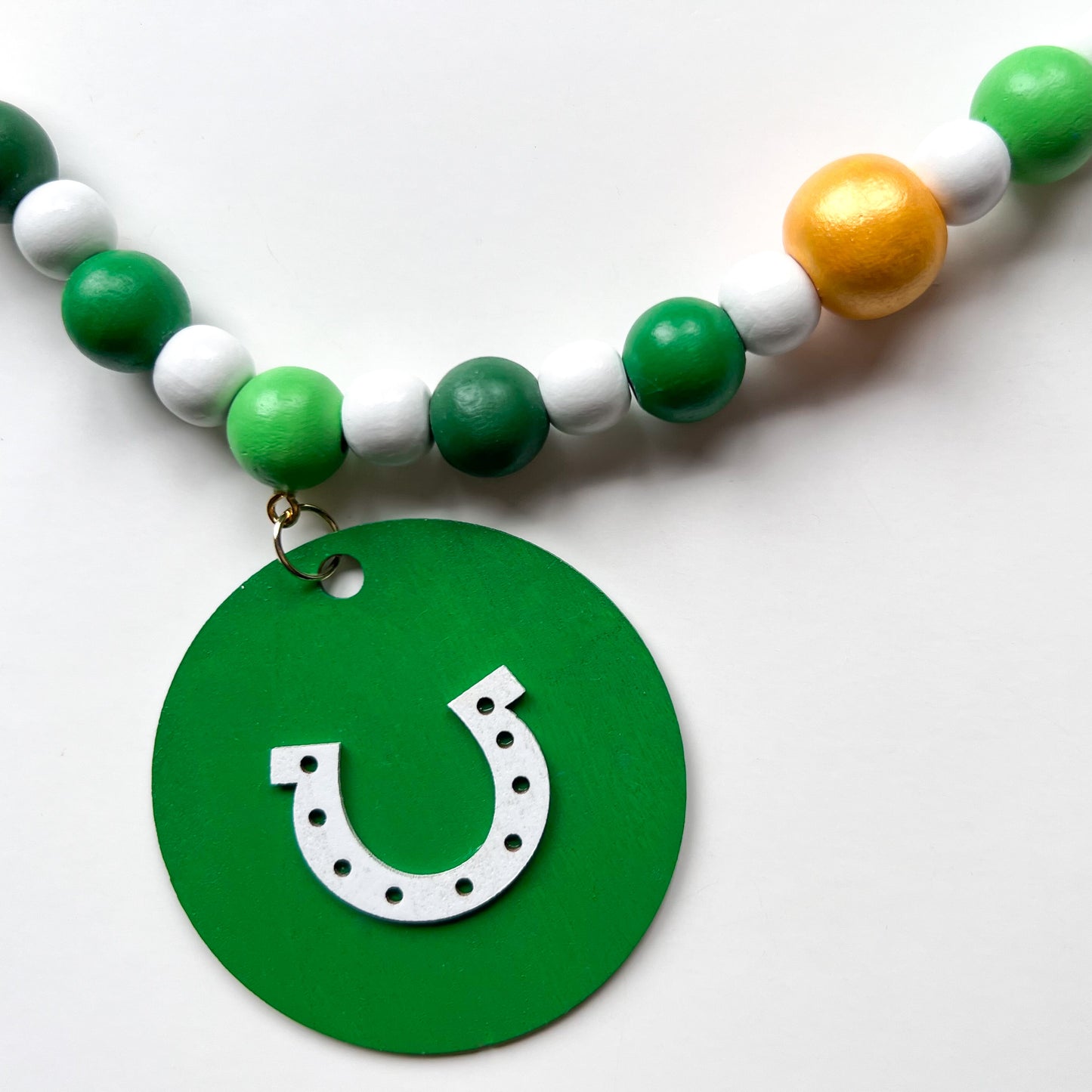 Lucky Clover Handmade Garland. The garland features five circles painted in three vibrant shades of green with white St. Patrick's Day themed icons. Circles hang from painted wood beads. St. Patrick’s Day spring seasonal decoration or gift.