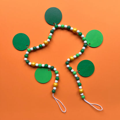 Lucky Clover Handmade Garland. The garland features five circles painted in three vibrant shades of green with white St. Patrick's Day themed icons. Circles hang from painted wood beads. St. Patrick’s Day spring seasonal decoration or gift.