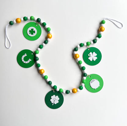 Lucky Clover Handmade Garland. The garland features five circles painted in three vibrant shades of green with white St. Patrick's Day themed icons. Circles hang from painted wood beads. St. Patrick’s Day spring seasonal decoration or gift.