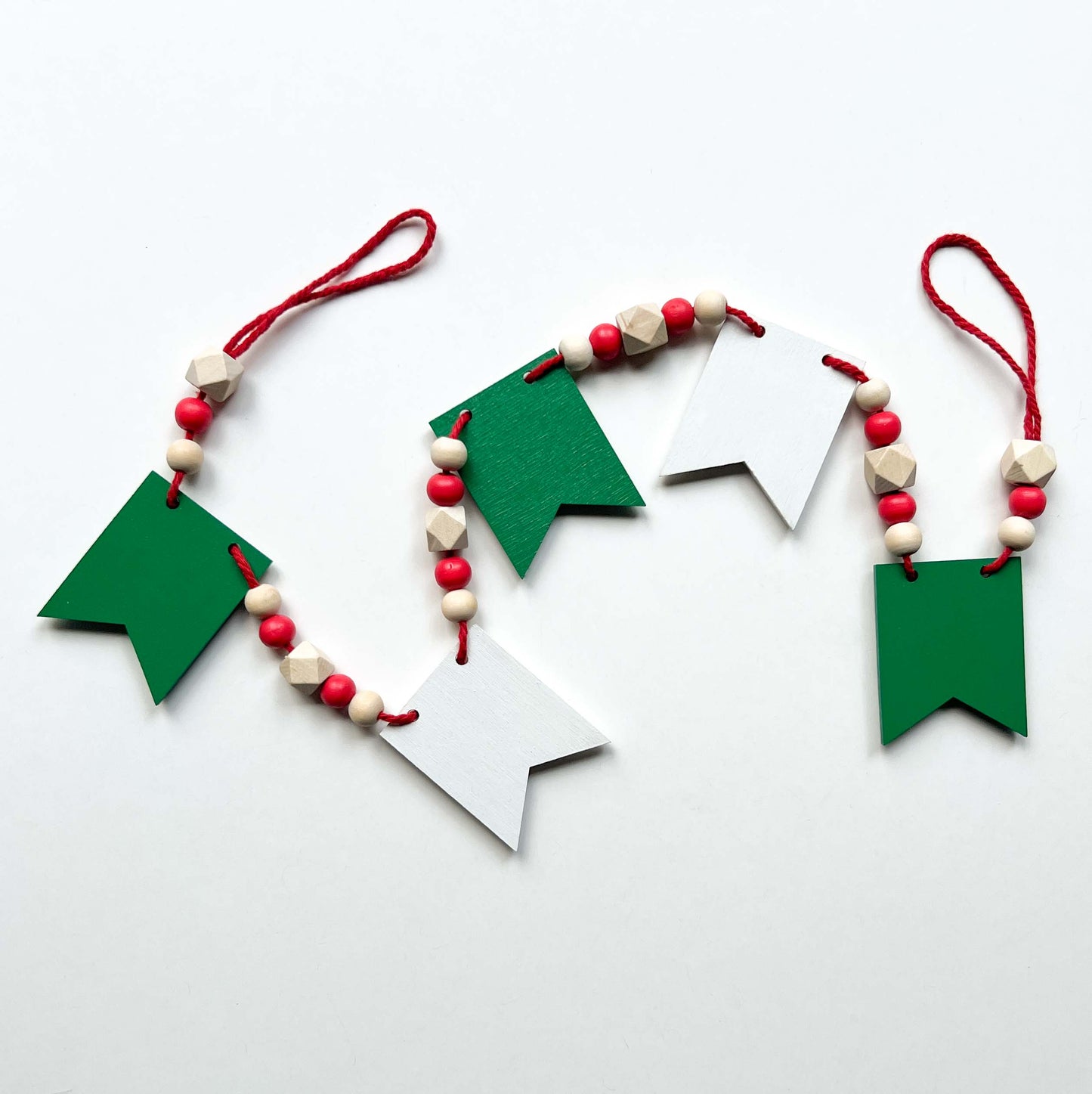 Christmas themed mini garland with pennants featuring Christmas items such as a tree, snowflake, gift, bells, and a rocking horse strung with natural and red beads.