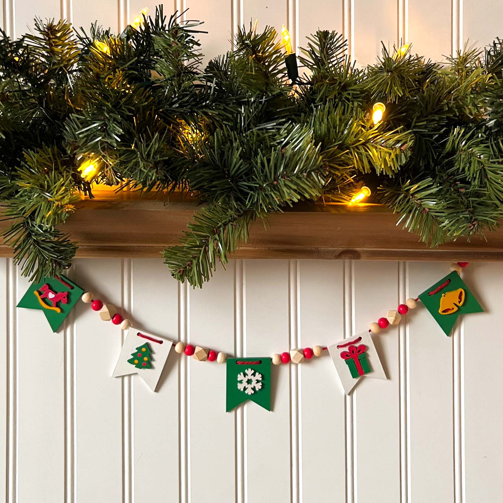 Christmas themed mini garland with pennants featuring Christmas items such as a tree, snowflake, gift, bells, and a rocking horse strung with natural and red beads.