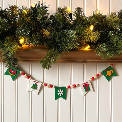 Christmas themed mini garland with pennants featuring Christmas items such as a tree, snowflake, gift, bells, and a rocking horse strung with natural and red beads.