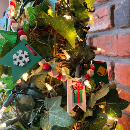 Christmas themed mini garland with pennants featuring Christmas items such as a tree, snowflake, gift, bells, and a rocking horse strung with natural and red beads.