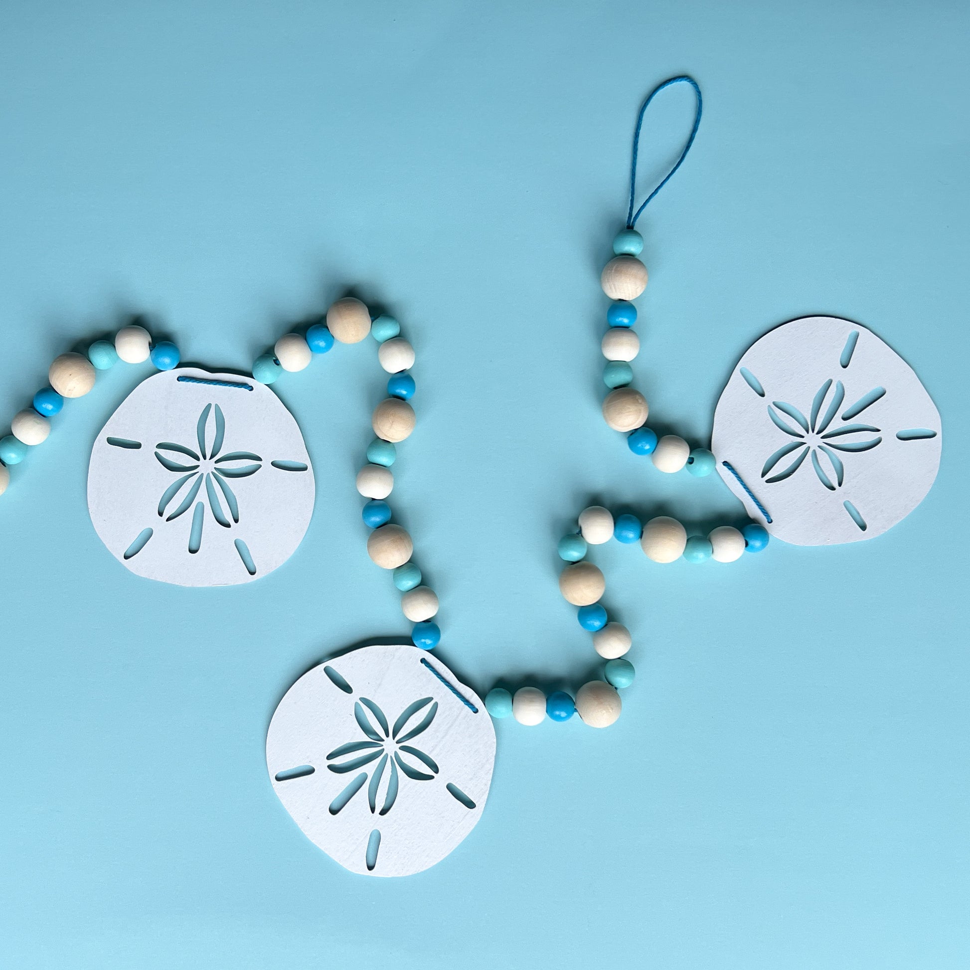 Seaside Sand Dollars Handmade Garland. The garland features three white sand dollars with blue and natural wood beads. Summer, ocean, beach theme decoration or gift.