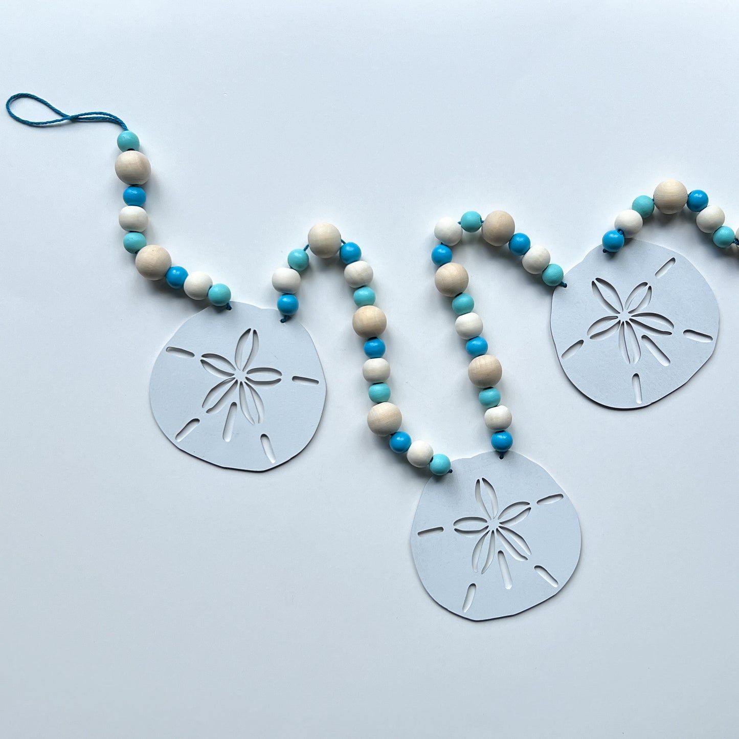 Seaside Sand Dollars Handmade Garland. The garland features three white sand dollars with blue and natural wood beads. Summer, ocean, beach theme decoration or gift.