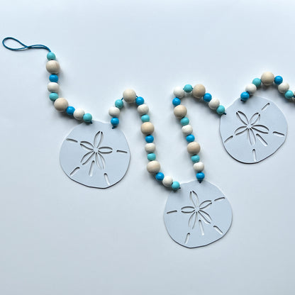 Seaside Sand Dollars Handmade Garland. The garland features three white sand dollars with blue and natural wood beads. Summer, ocean, beach theme decoration or gift.