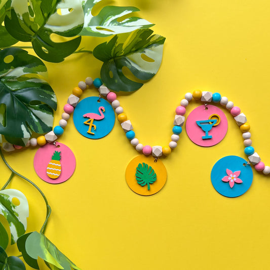 Tropical Little Vacay Mini Garland. Features wood shapes of a pineapple, flamingo, leaf, drink, and flower. Wood bead garland for summer, tropical theme decor or gift.
